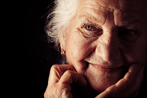 Close up of elderly woman softly smiling with brown eyes and a dark background