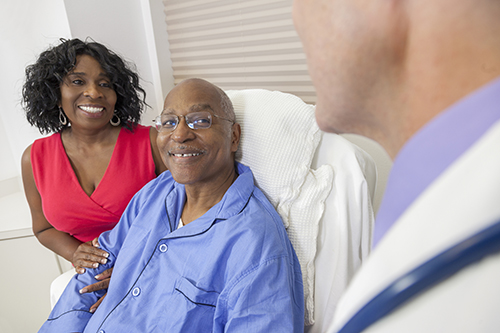 Smiling patient in hospital bed with wife in red top smiling beside him